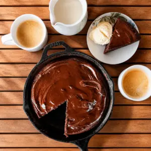 Kaffee Schoko Kuchen in einer gusseisernen Pfanne mit Schokoglasur, dazu eine Tasse Kaffee und ein Stück Kuchen mit Vanilleeis